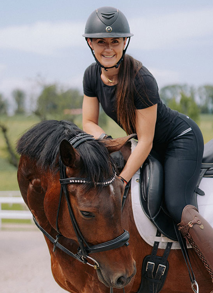 Eine lächelnde Trainerin sitzt auf einem Pferd mit Reitausrüstung